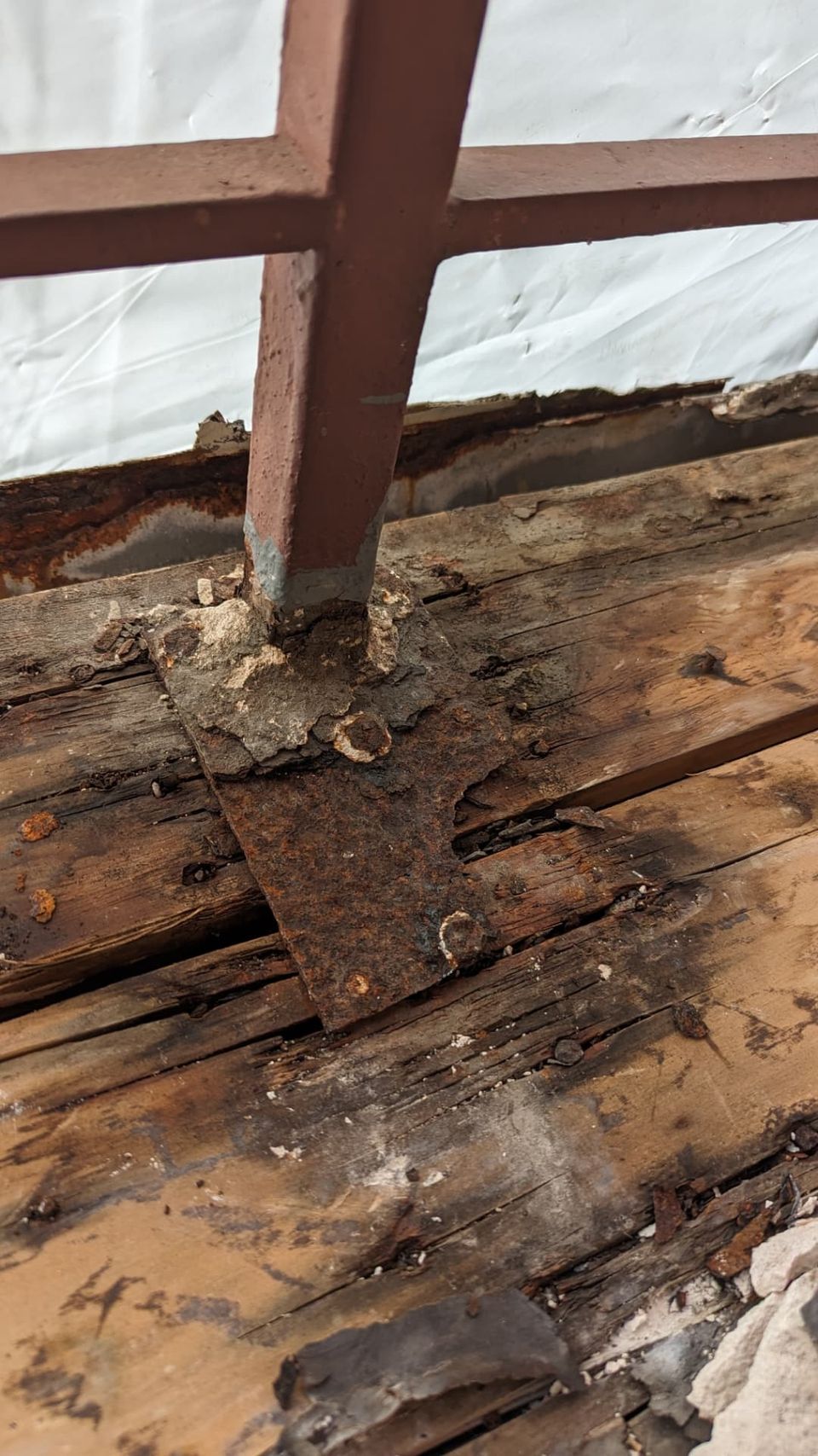 Close-up of corroded metal and deteriorated wood at an apartment walkway railing base.