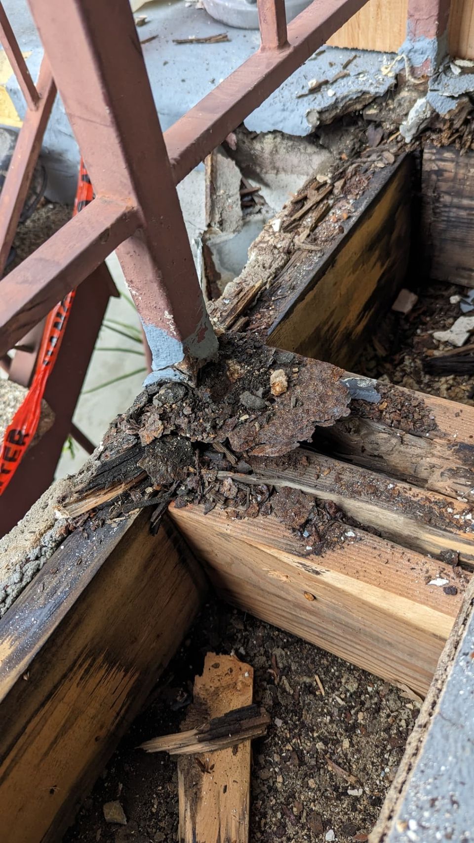 Close-up of damaged wood and corroded metal at an apartment walkway railing attachment.