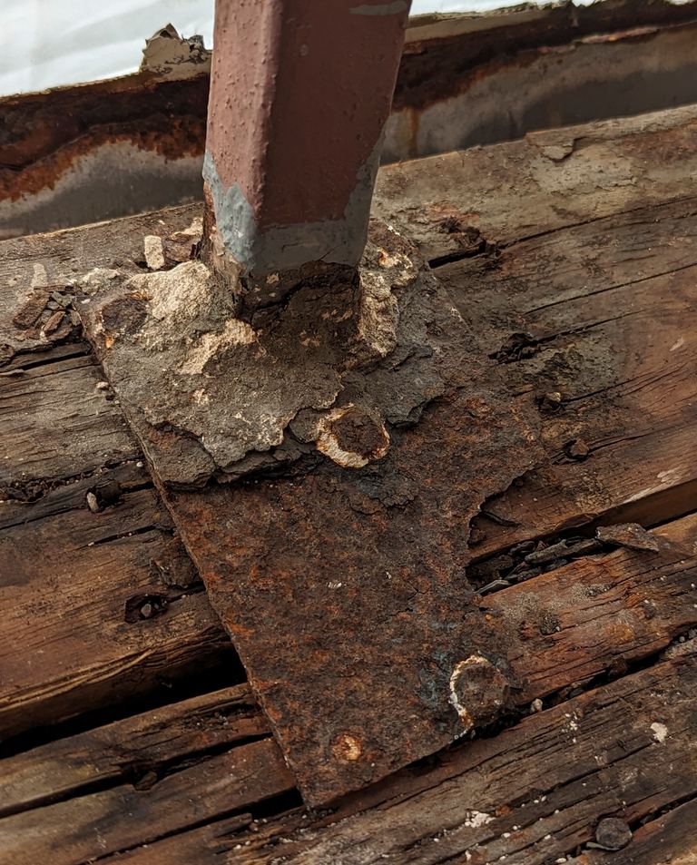 Rusted railing post base plate corroded through on a wood balcony deck — hidden structural failure beneath waterproofing